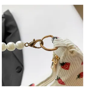 Detail of white corduroy crescent bag with strawberry print and pearl bead strap