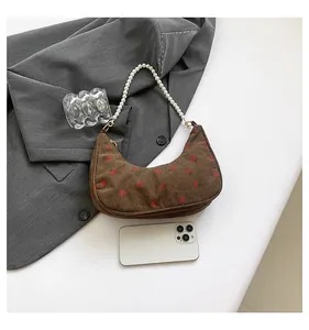 Close-up of brown corduroy crescent bag with strawberry embroidery and pearl strap