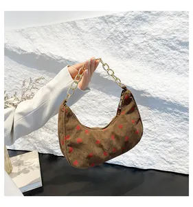 Close-up of brown corduroy crescent bag with red strawberry print and gold chain handle
