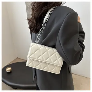 Close-up of beige quilted crossbody bag with silver chain strap worn by a model
