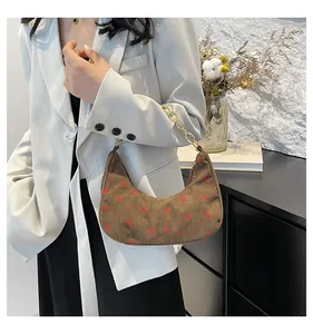 Detail of a brown corduroy crescent bag featuring red strawberry prints and a gold chain