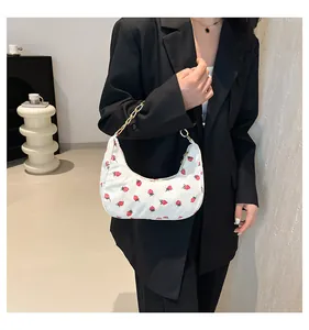 Detail of white corduroy crescent bag with strawberry prints and a gold chain strap