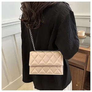 Rear view of a model wearing a beige quilted crossbody bag with a silver chain strap