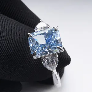 3 carat radiant cut light blue stone ring with heart side stones in silver claw setting