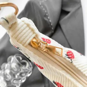 White corduroy crescent bag with red strawberry print and gold metal zipper detail
