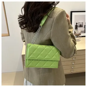 Detail of green quilted crossbody bag with silver chain strap shown on a shoulder