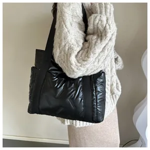 Detailaufnahme einer schwarzen Stepp-Tragetasche mit Glanzeffekt an einem Strickpullover