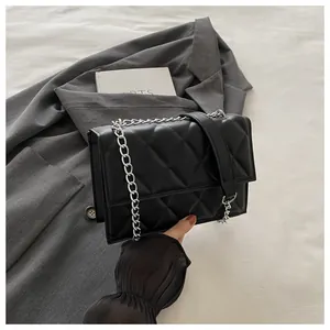 Detail of black quilted shoulder bag with silver chain strap on a grey blazer