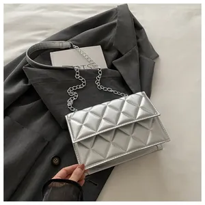Detailed close-up of silver quilted crossbody bag with metal chain strap on grey blazer