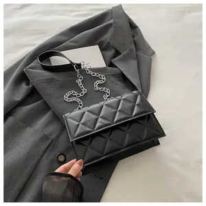 Close-up of quilted black leather shoulder bag with silver chain on a grey blazer