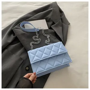 Detail of light blue quilted crossbody bag with silver chain strap on grey blazer