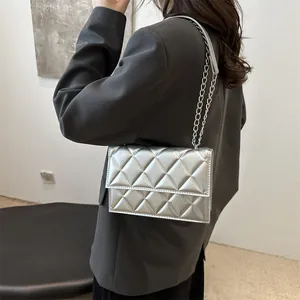 Chic silver quilted shoulder bag with metal chain strap worn by a model in a modern room