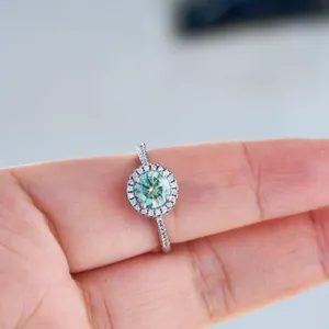 Silver halo ring with round teal moissanite stone shown on person finger