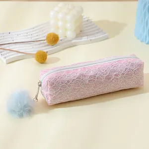 Trousse à crayons en dentelle rose avec pompon bleu sur fond crème et accessoires