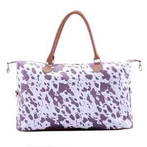 Détail du sac de voyage avec imprimé vache violet, anses brunes et finitions dorées