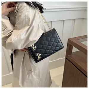 Détail du sac à bandoulière matelassé avec nœuds dorés sur un trench-coat beige