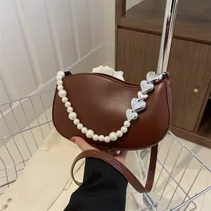 Chic brown half-moon crossbody bag with elegant pearl strap and silver heart buckles