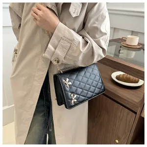 Détail du motif matelassé et des nœuds dorés sur un sac à bandoulière noir porté avec un manteau