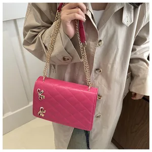 Détail du sac bandoulière matelassé fuchsia avec nœuds dorés et bandoulière en chaîne