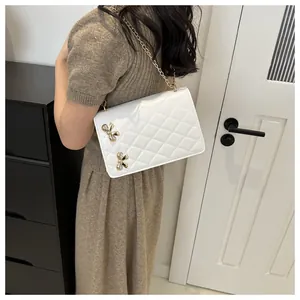 Détail d'un sac bandoulière matelassé blanc avec chaîne dorée et boucles en métal nœud