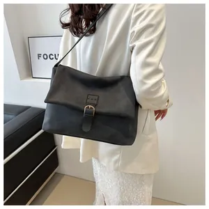 Gros plan d'un sac cabas en cuir mat noir avec boucle dorée porté à l'épaule sur mannequin