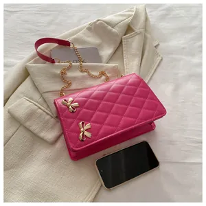 Détail d'un sac bandoulière fuchsia matelassé avec nœuds dorés et bandoulière chaîne