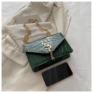 Detail einer dunkelgrünen Handtasche mit Steinstruktur, Goldlogo und Fransen