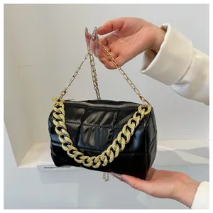 Detail of black quilted cylindrical handbag with chunky gold chain and leather texture