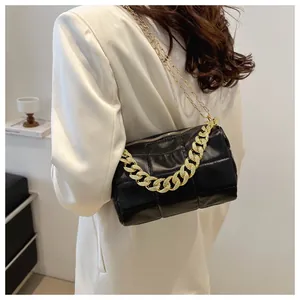 Detail of black quilted shoulder bag with bold gold chain handle and slim chain strap