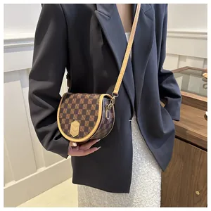 Detailed view of vintage checkered saddle bag with adjustable leather strap worn by model