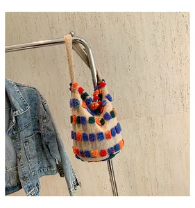 Detail of plush knit bucket bag with colorful square pom-poms on a beige surface