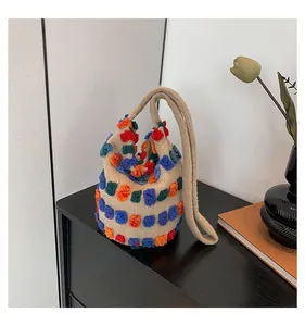 Detail of colorful plush pom-pom charms on a beige hand-crocheted bucket bag strap