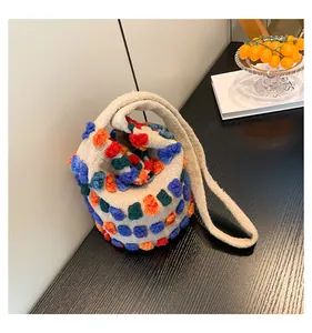 Detail of beige plush bucket bag featuring colorful textured 3D pom-poms on black desk