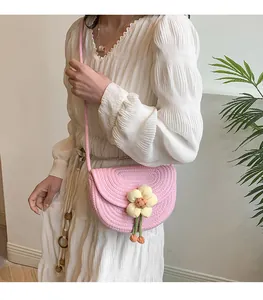 Detalle del bolso bandolera trenzado rosa con flor amarilla sobre vestido blanco