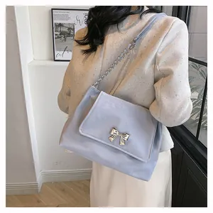Close-up of a blue shoulder bag with a silver bow buckle on beige tweed fabric