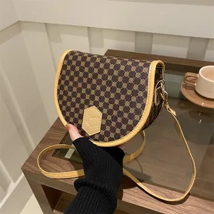 Retro monogram saddle bag with brown floral pattern and adjustable leather strap on wood