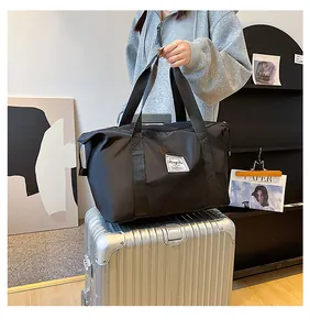 Detail of waterproof black travel bag with double handles placed on top of silver suitcase