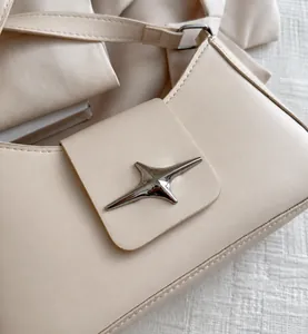 Detail view of a metallic star emblem on a minimalist cream white shoulder underarm bag