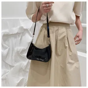 Sac sous le bras en cuir verni noir brillant porté par un mannequin avec une tenue
