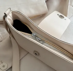 Detail view of smooth metal zipper and magnetic closure on cream underarm shoulder bag