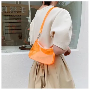 Détail d'un sac demi-lune en PVC orange transparent porté à l'épaule sous le soleil
