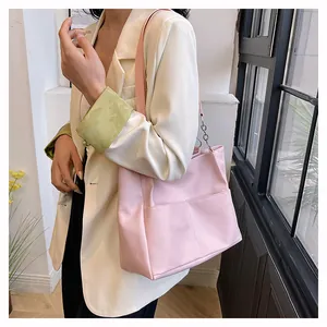 Detail of soft pink oversized tote bag with functional front pockets worn with a beige blazer