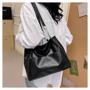 Detail of black faux leather tote bag with metallic chain strap and front pockets