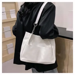 White faux leather tote bag with exterior pockets and silver chain detail on model