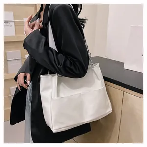 Detail view of large white tote bag featuring a front pocket and metal chain strap