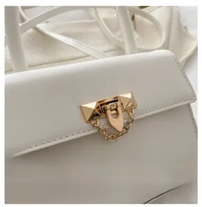 Detail of white handbag featuring gold-tone clasp, pyramid studs and chain decoration