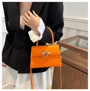 Detail of bright orange square crossbody bag with gold rivet lock and chain strap on model