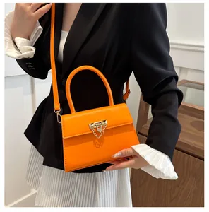 Close-up of vibrant orange crossbody bag featuring a golden lock and pyramid studs