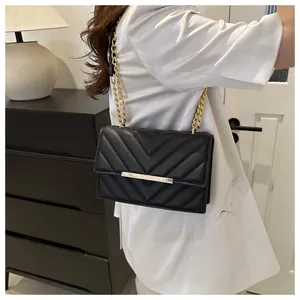 Dettaglio di borsa nera in pelle trapuntata a V con catena dorata indossata da una modella