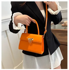 Detail of bright orange crossbody bag featuring a golden metal buckle and chain decoration